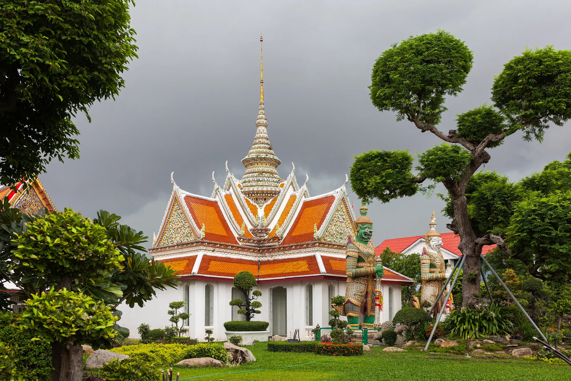 Wat Arun in Bangkok met oranje en witte daken, bonsai-achtige bomen en reuzenwachters