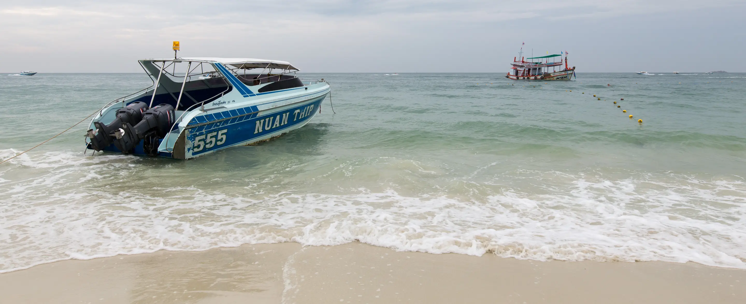 Een speedboot ligt in de branding voor het strand van Ko Samet, met in de verte een vissersboot