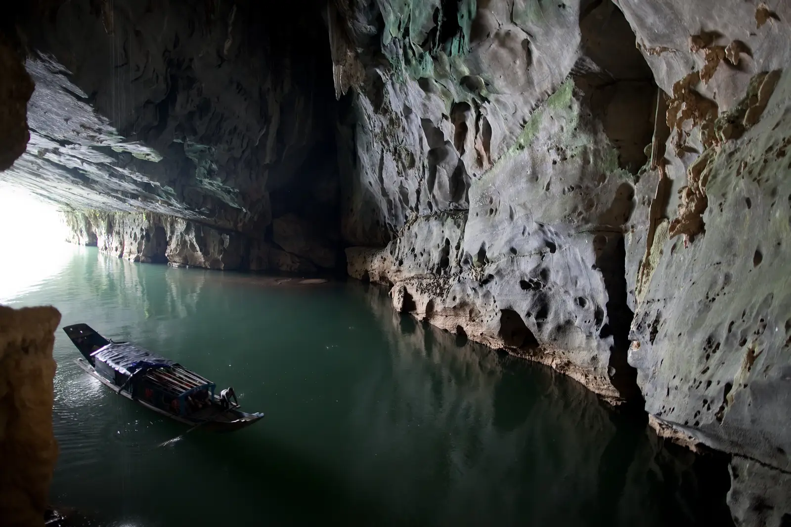 Een boot vaart de rivier op bij de ingang van de Phong Nha-grot, tussen donkere rotswanden