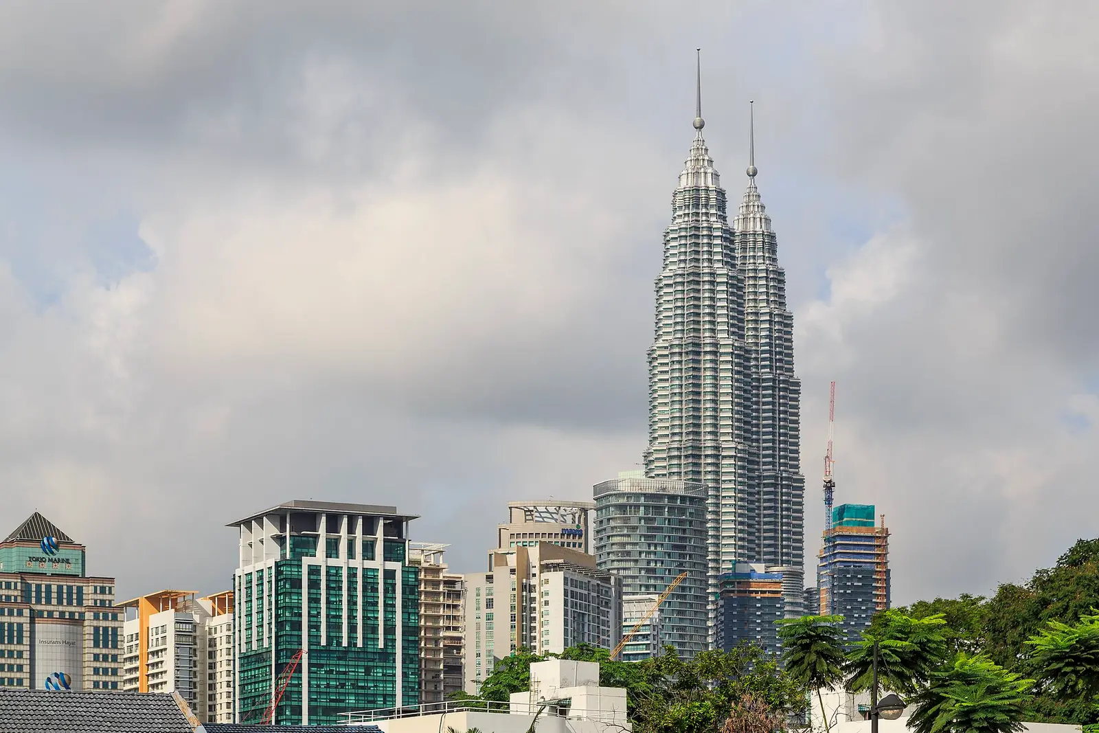De Petronas Twin Towers in Kuala Lumpur boven andere hoogbouw, onder een bewolkte lucht