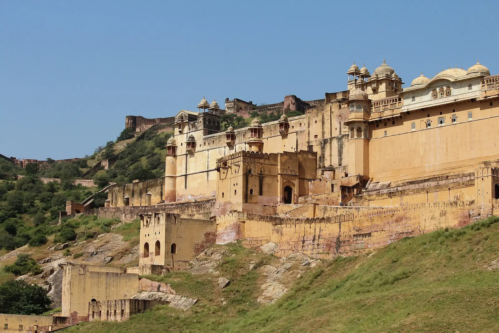 De muren en torentjes van Amber Fort tegen een helling bij Jaipur, onder een blauwe lucht