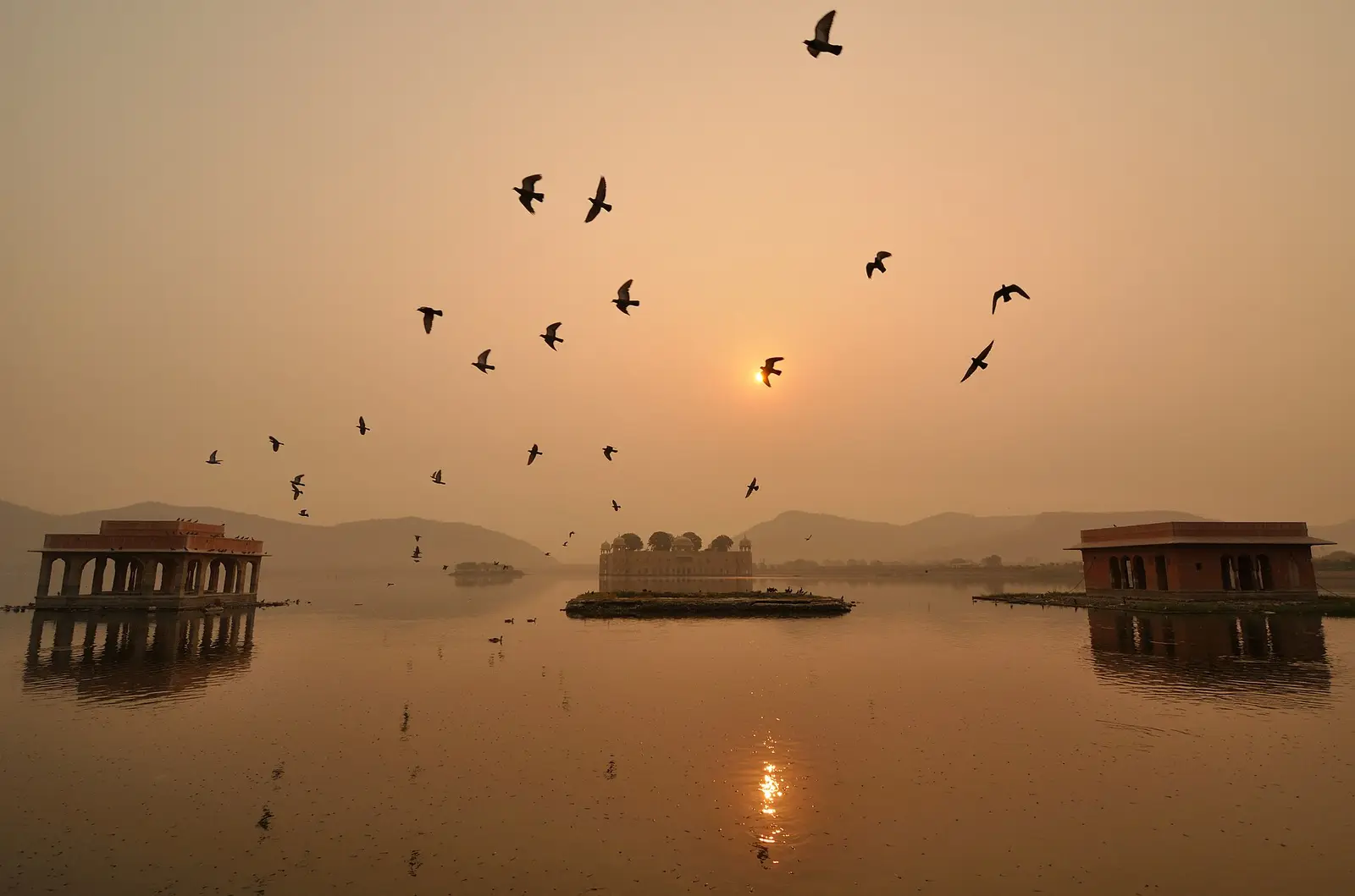 Het Jal Mahal in het Man Sagar-meer bij zonsopkomst, met vogels in de lucht