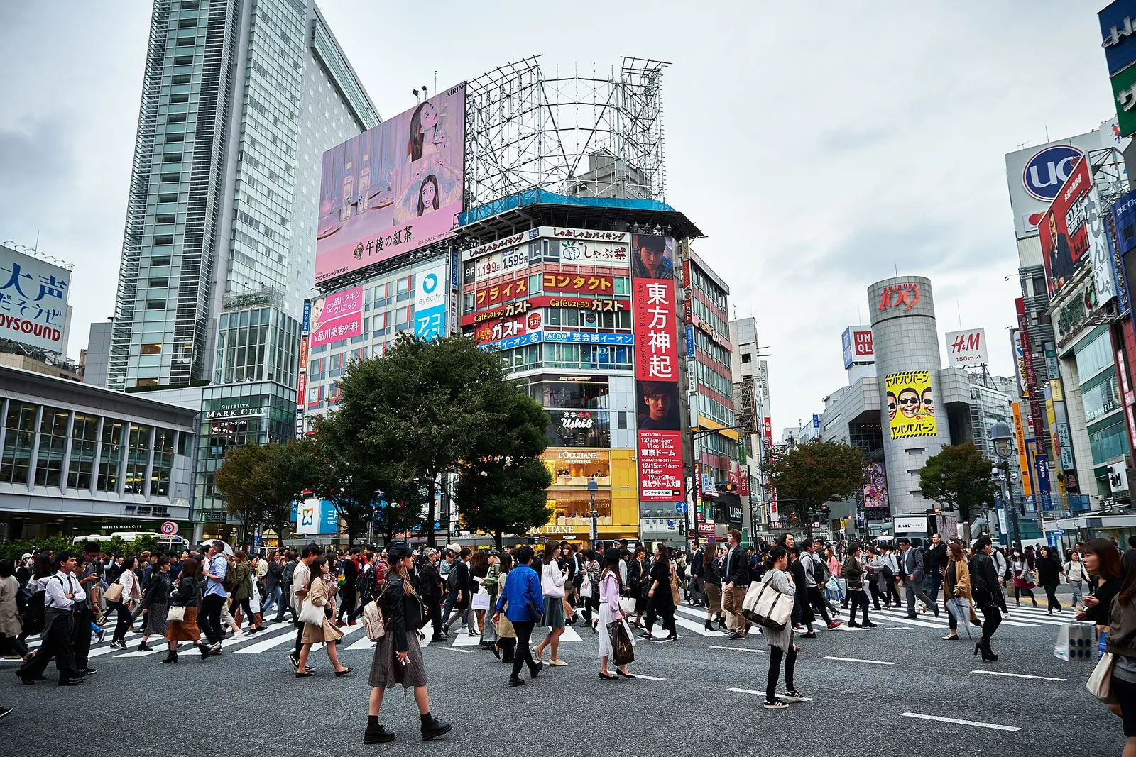 Voetgangers steken het grote kruispunt bij station Shibuya over, tussen hoge gebouwen met reclameschermen