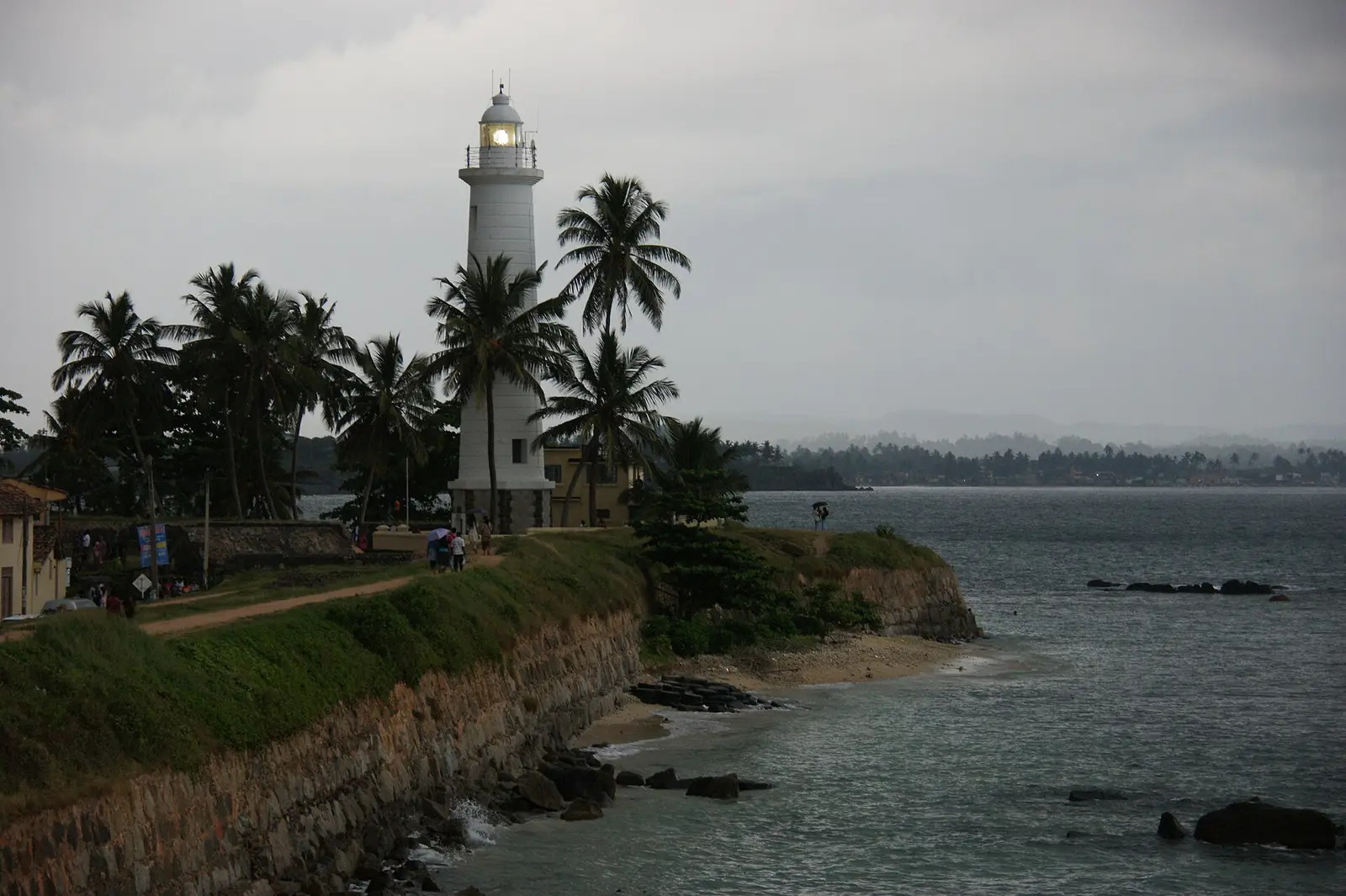 De witte vuurtoren van Galle Fort bij schemering, met palmbomen en de zee ernaast