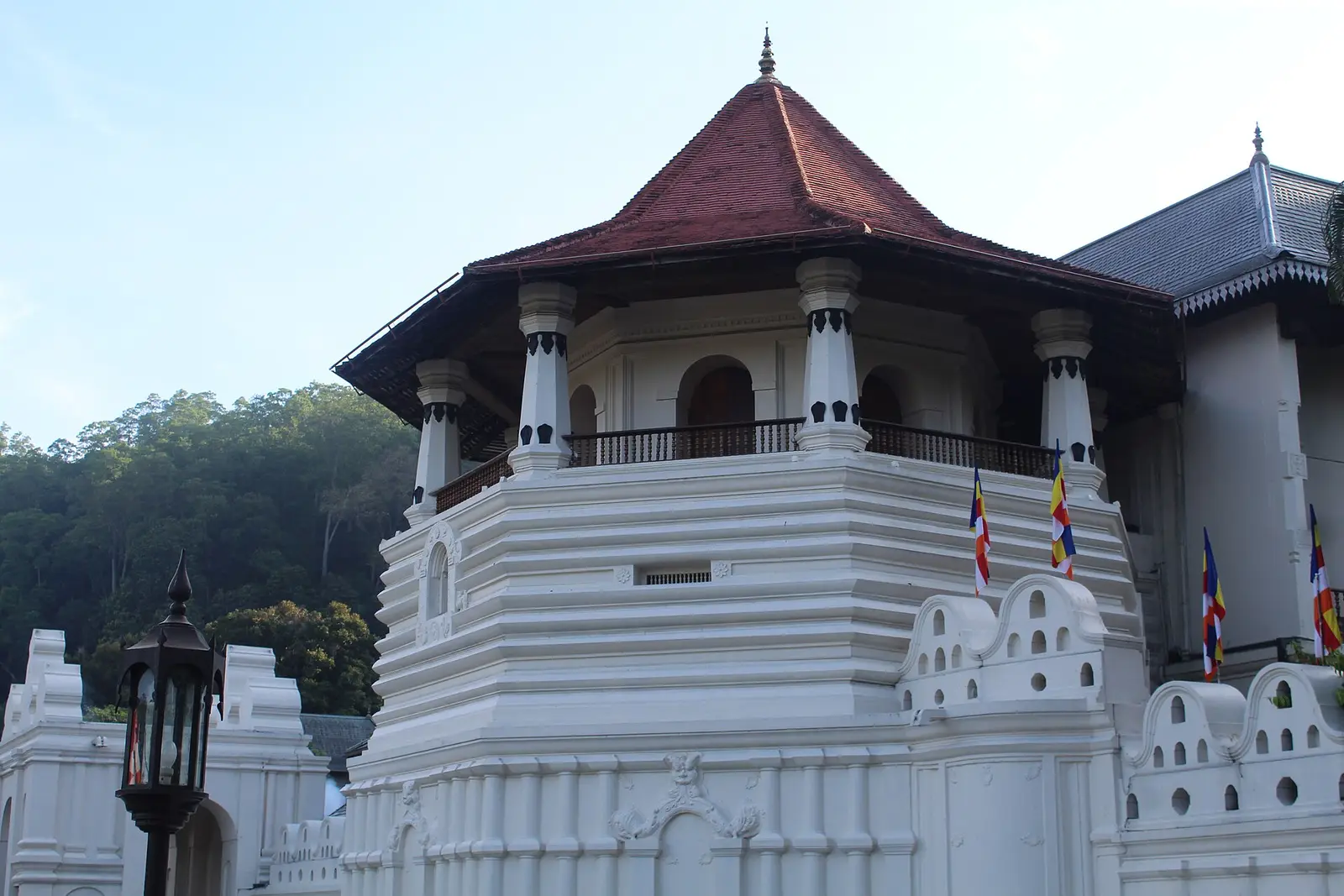 De achthoekige toren van de Tempel van de Tand in Kandy met een rood dak, tegen een beboste heuvel