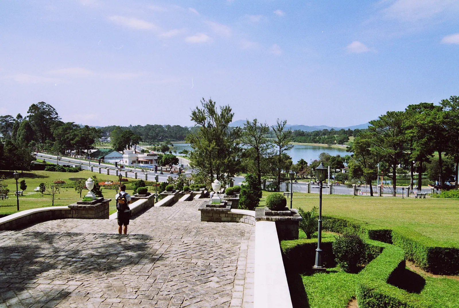 Uitzicht over een trap en tuin naar het Xuan Huong-meer in Da Lat, met dennen langs de oever