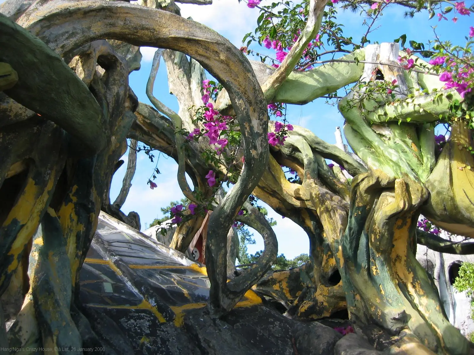 Slingerende betonnen takken en bougainvillea van de Crazy House in Da Lat, tegen een blauwe lucht