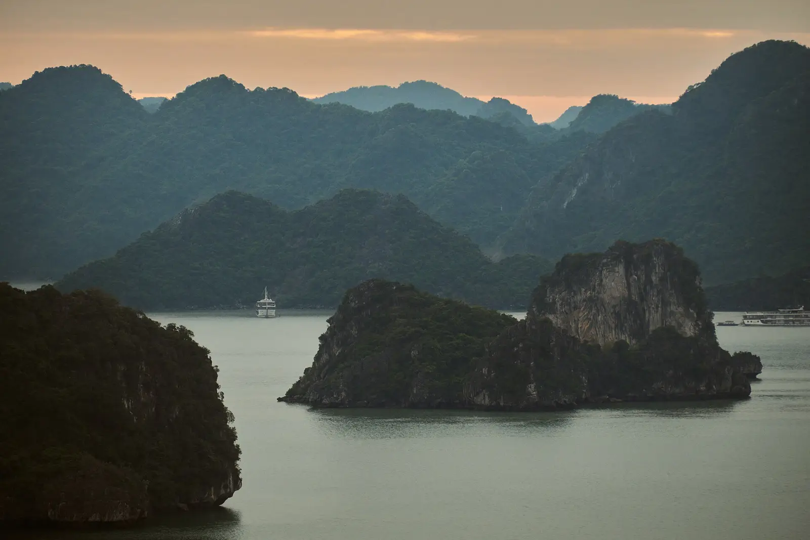 Kalksteeneilanden in de baai van Ha Long in de schemering, met een boot op het water