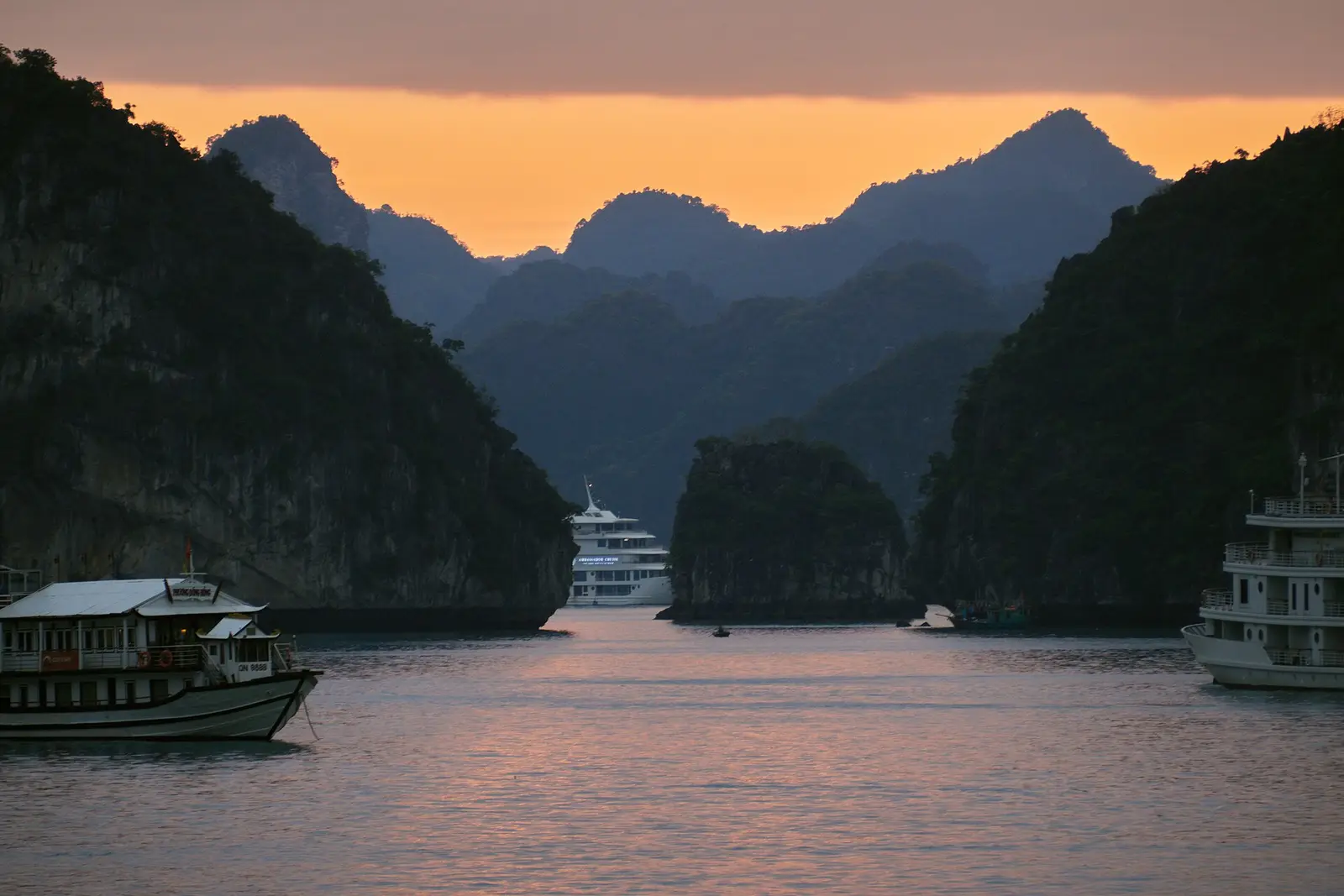 Kalksteeneilandjes in de baai van Ha Long bij zonsondergang, met toeristenboten op het water