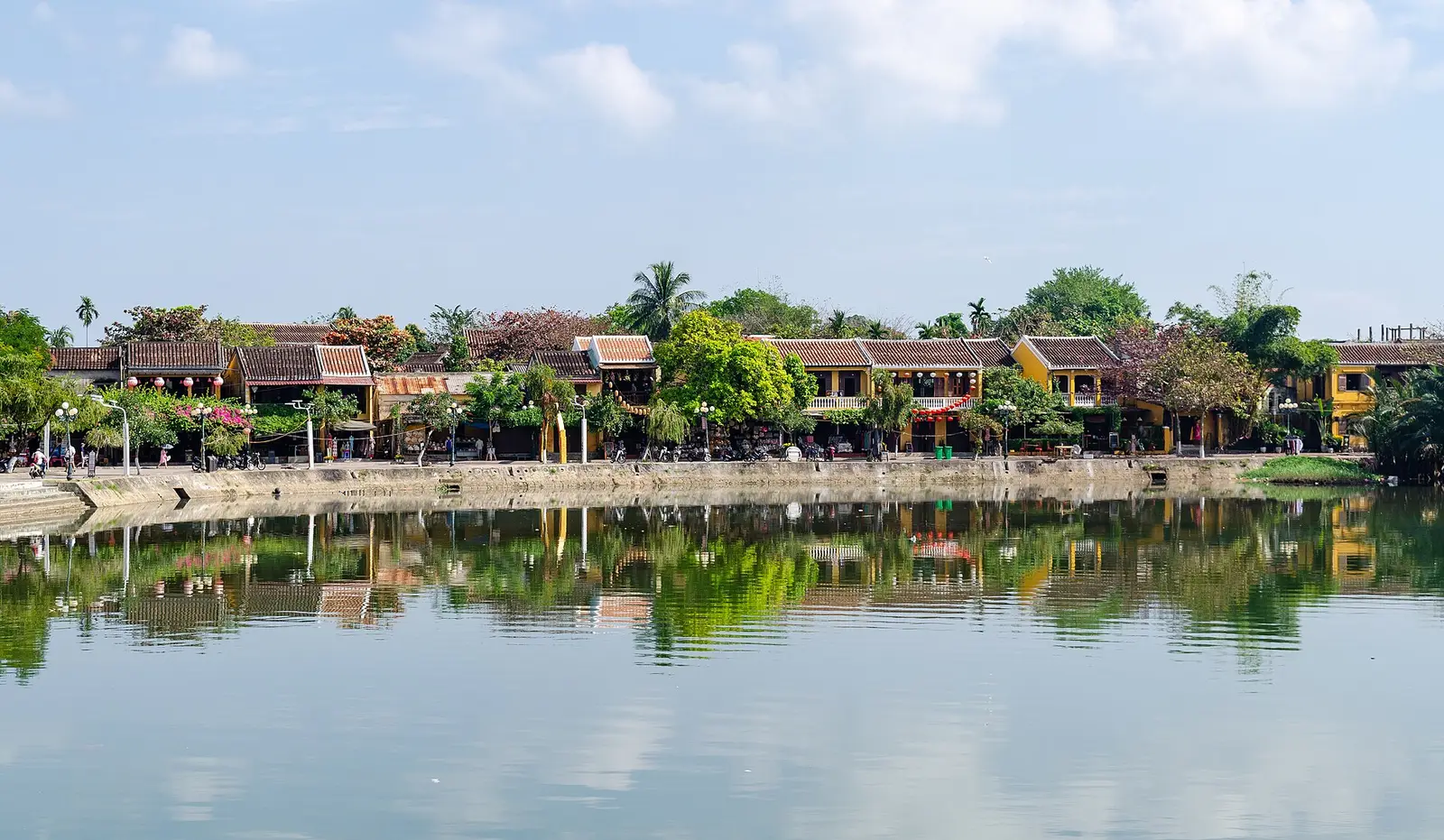 Gele huizen en bomen aan de rivier in de oude stad van Hoi An, weerspiegeld in het water