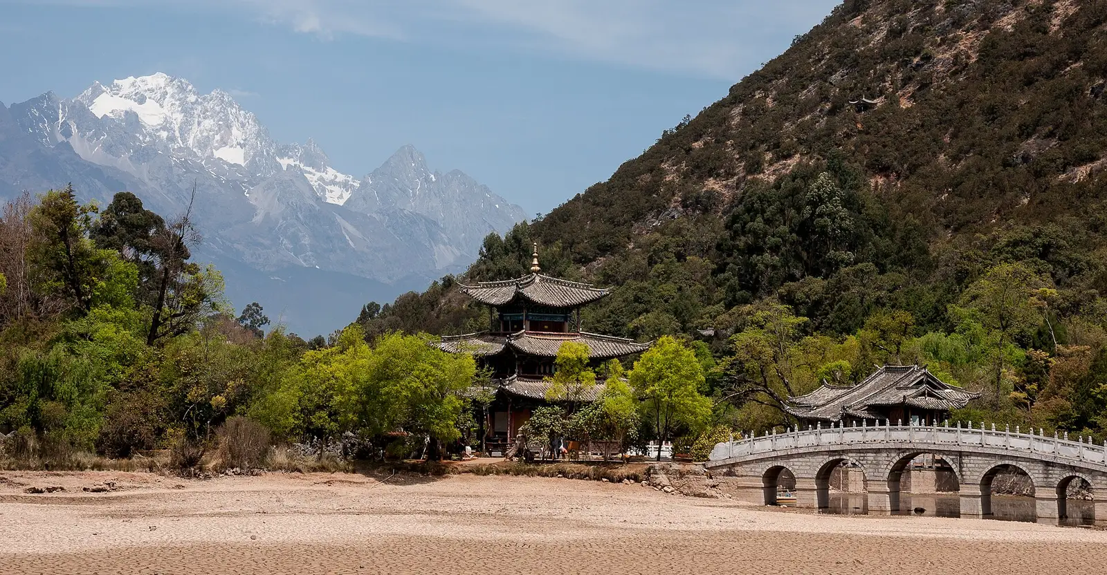 Een paviljoen en een stenen brug bij de Zwarte Drakenvijver in Lijiang, met de besneeuwde Jade Draak-berg erachter